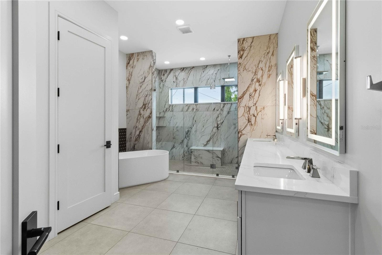 Floor-to-ceiling marble tile surrounds the oversized glass-enclosed shower, while a freestanding soaking tub, dual vanities, illuminated mirrors, contemporary fixtures, and a dedicated makeup station bring boutique-hotel luxury into everyday life - 104 S MAKI RD, PLANT CITY