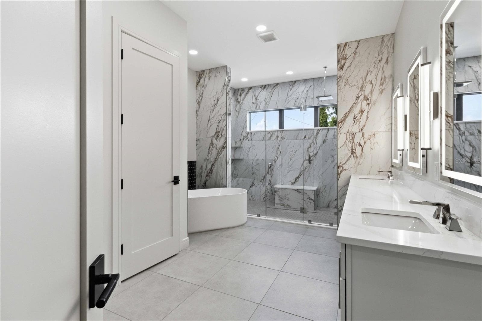 Floor-to-ceiling marble tile surrounds the oversized glass-enclosed shower, while a freestanding soaking tub, dual vanities, illuminated mirrors, contemporary fixtures, and a dedicated makeup station bring boutique-hotel luxury into everyday life - 104 S MAKI RD, PLANT CITY