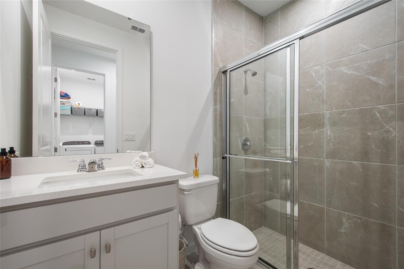 Hall bath adjacent to Bedroom 4 has a walk in shower with floor to ceiling tile and a sliding door for easy access. Single vanity has quartz countertops and a lovely transitional design. - 2685 SWEET ACACIA DR, CLERMONT