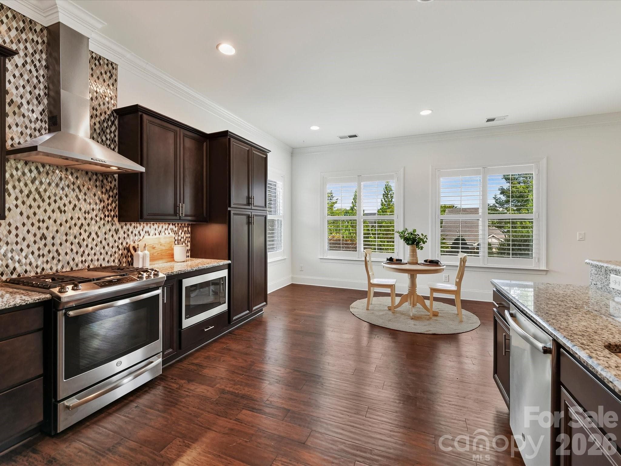 Spacious kitchen features granite countertops, abundant cabinetry, stainless steel appliances, a gas range with vent hood, decorative tile backsplash, and an expansive breakfast bar with seating. - 13003 Riley Grace Lane, Cornelius