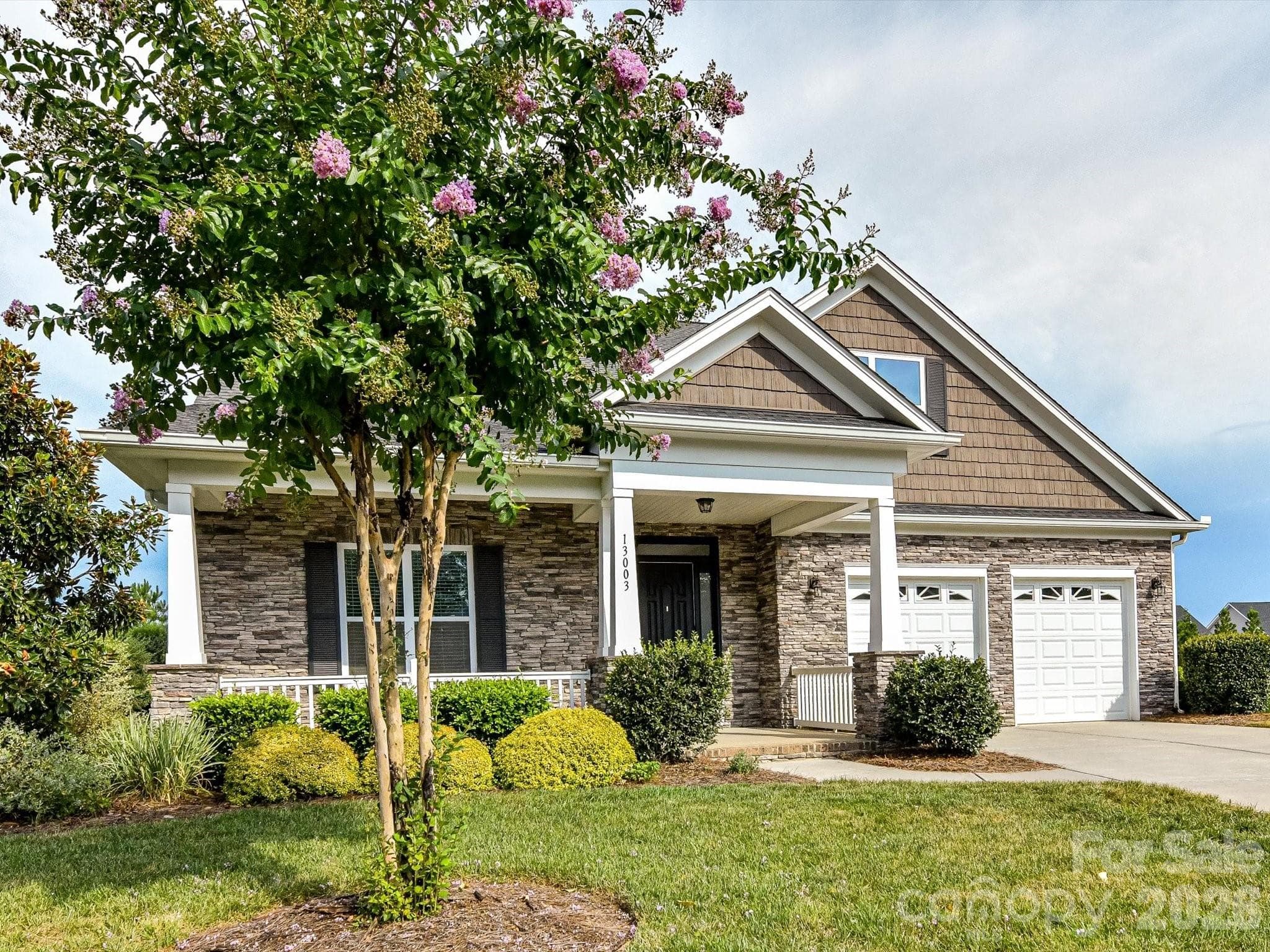 Beautifully maintained home offers charming curb appeal with stone accents, a welcoming covered front porch, manicured landscaping, and a two-car garage. - 13003 Riley Grace Lane, Cornelius