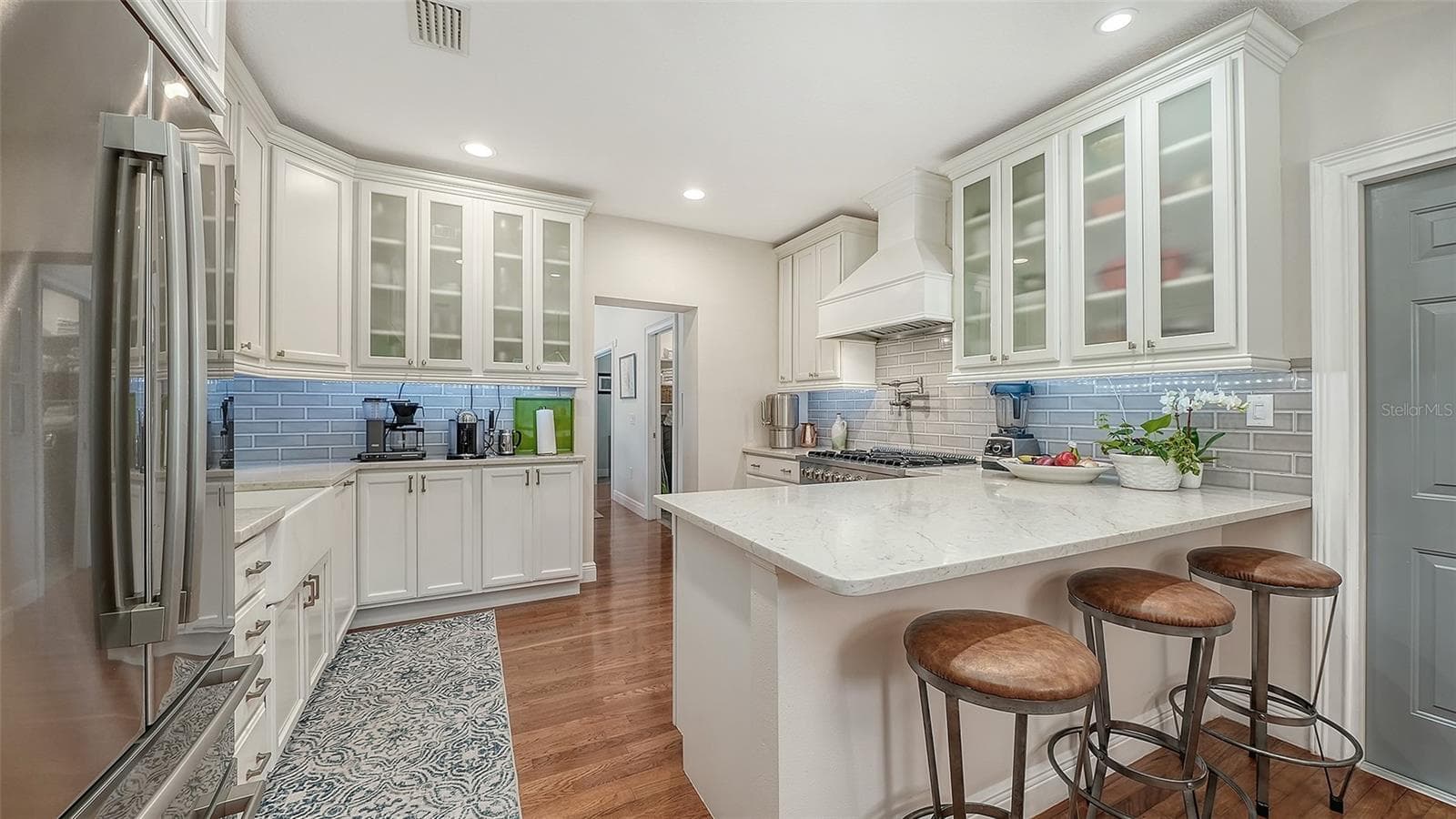 Bright gourmet kitchen showcases custom cabinetry, glass-front storage, quartz surfaces, and an oversized island with seating. - 1685 6TH ST, SARASOTA
