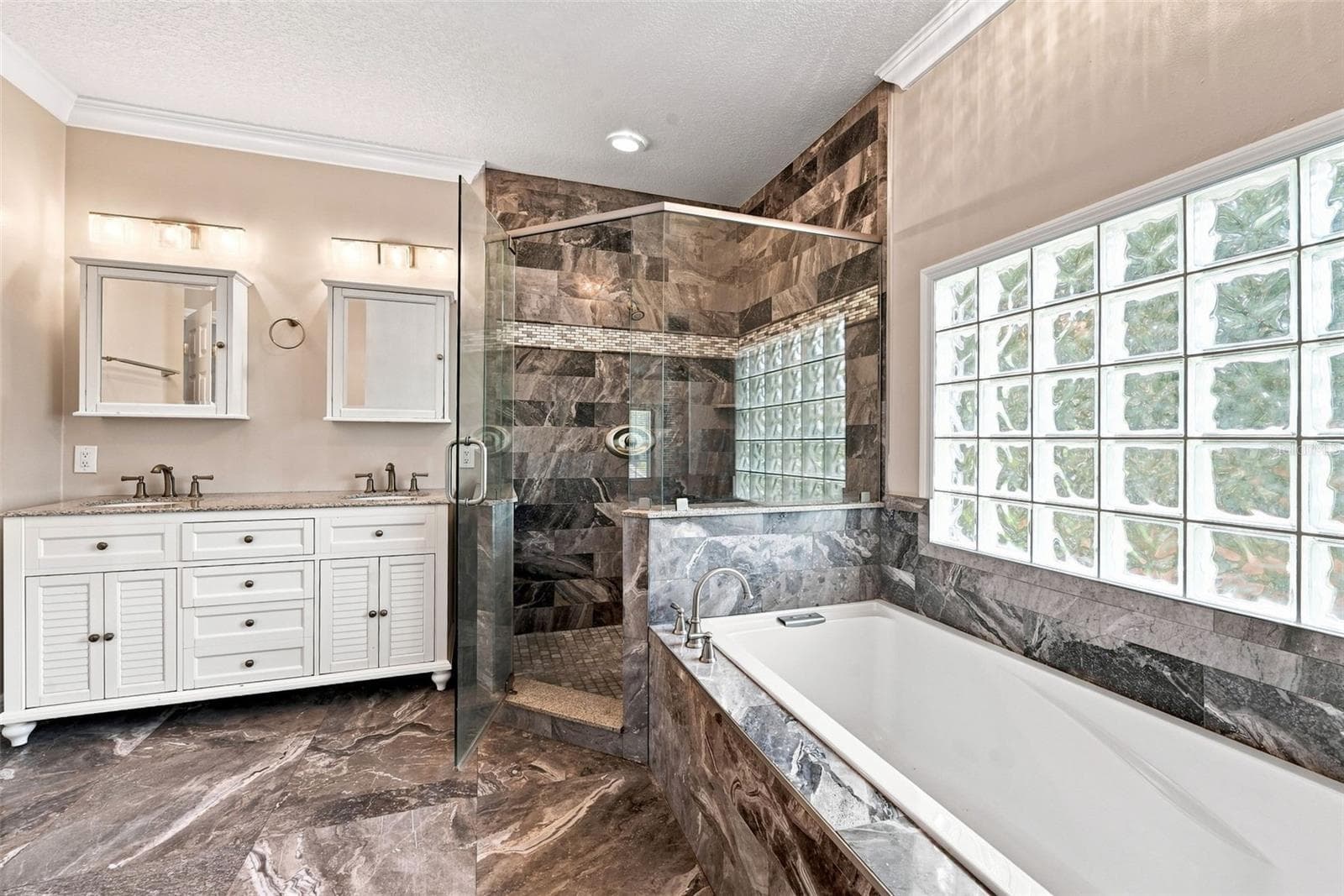 Luxurious Primary Bathroom showcases dual vanities, large soaking tub, walk-in shower, decorative tile, and glass-block natural lighting. - 1349 VALLEY PINE CIR, APOPKA