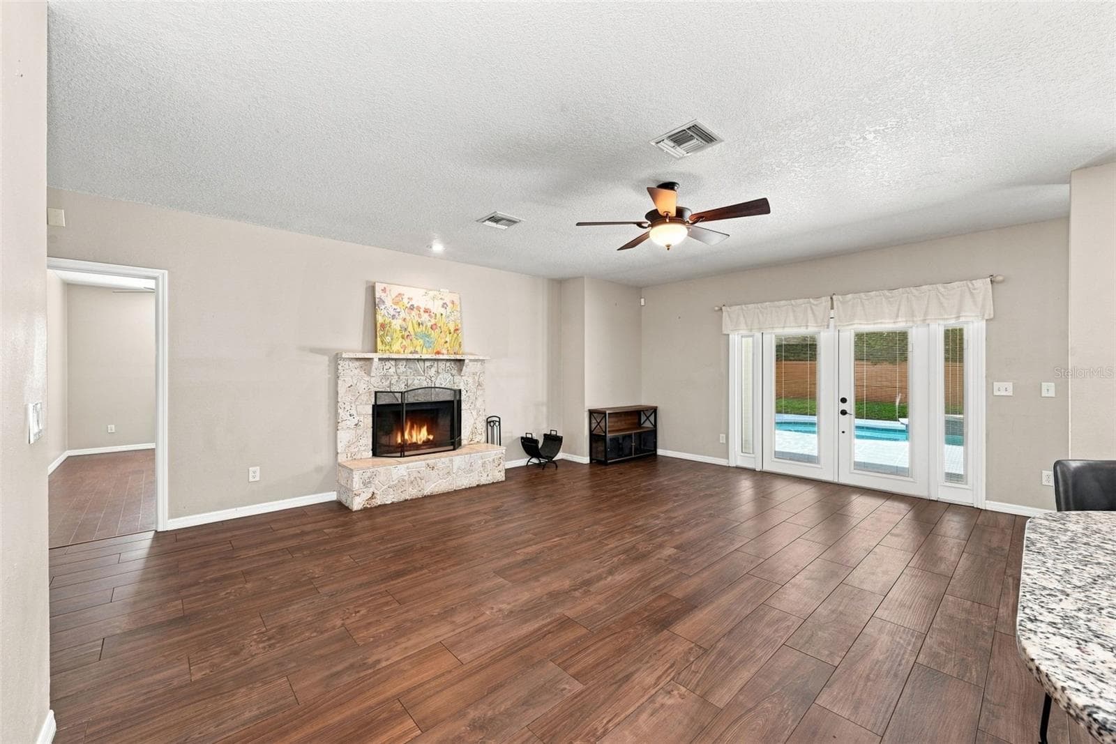 Spacious Family Room with Wood-Burning Fireplace offers generous gathering space, beautiful wood flooring, French doors, and views toward the pool. - 1349 VALLEY PINE CIR, APOPKA