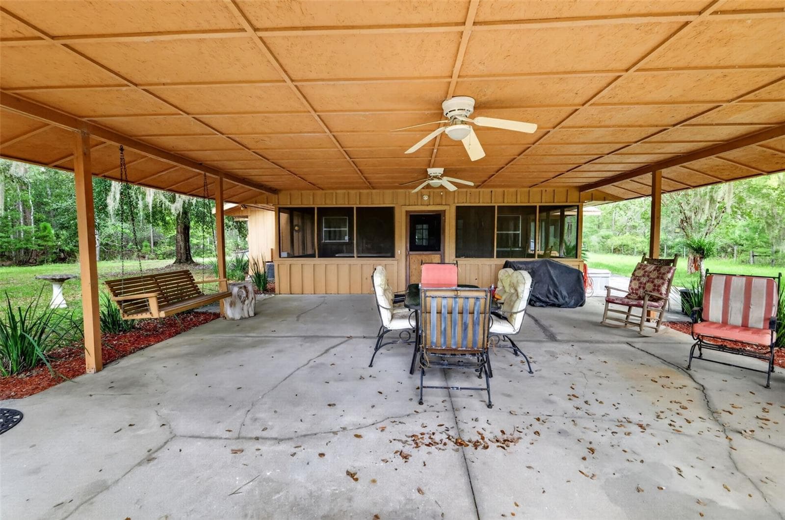 Long view of 23' x 23' covered porch with ceilings fans, porch swing and planting beds - 24939 OLD DEER RD, PAISLEY