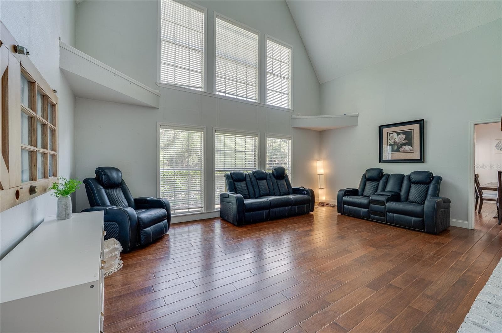 Grand living room highlighted by soaring vaulted ceilings, warm laminate floors, and a double-stacked bank of large windows offering abundant natural light. - 2081 PENNSYLVANIA DR, DELAND