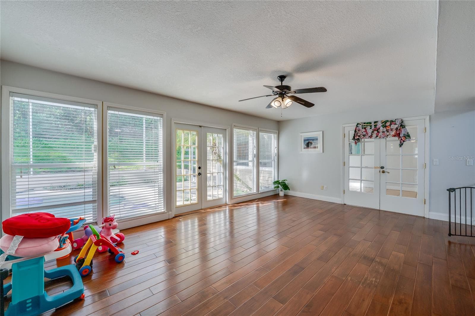 Open living area featuring rich laminate floors, a central ceiling fan, and multiple paned windows and glass doors opening to the outdoor pool patio. - 2081 PENNSYLVANIA DR, DELAND