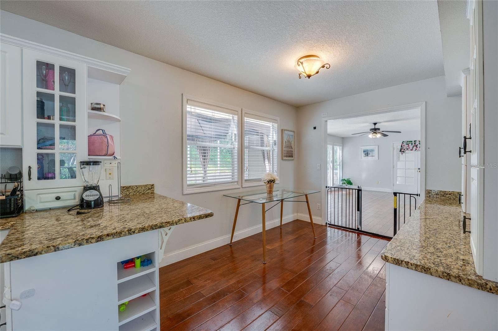 Functional kitchen nook featuring granite countertops, white cabinetry with display shelving, and rich laminate flooring. - 2081 PENNSYLVANIA DR, DELAND