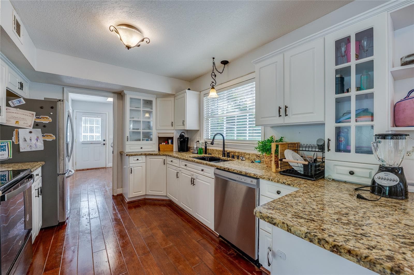 Bright, spacious kitchen showcasing white cabinetry, speckled granite countertops, stainless steel appliances, and rich laminate flooring. - 2081 PENNSYLVANIA DR, DELAND