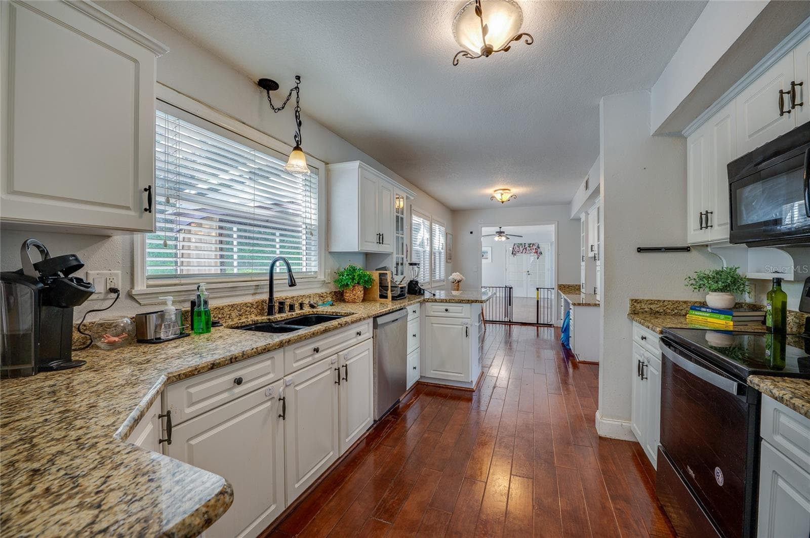 Long galley-style kitchen featuring granite countertops, crisp white cabinets, a black sink basin, and an open sightline through the home. - 2081 PENNSYLVANIA DR, DELAND