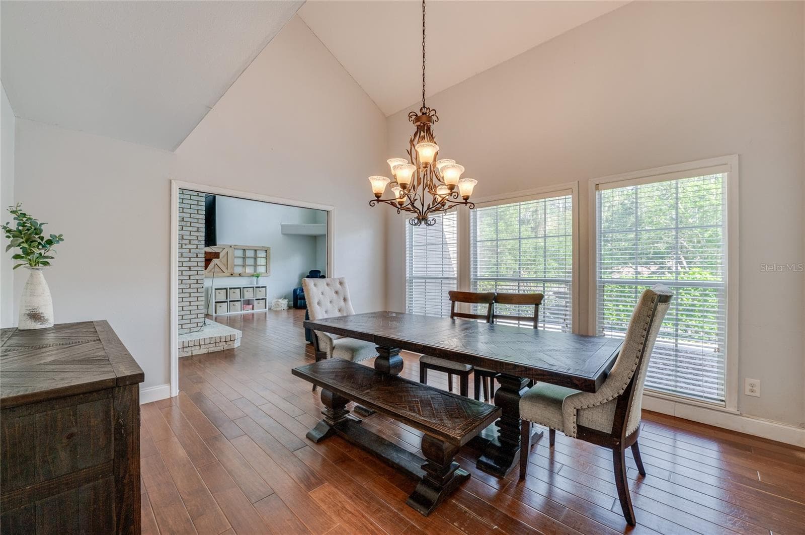 Open dining space featuring high ceilings, warm laminate floors, a classic chandelier, and a wide doorway connecting into the adjoining living room. - 2081 PENNSYLVANIA DR, DELAND