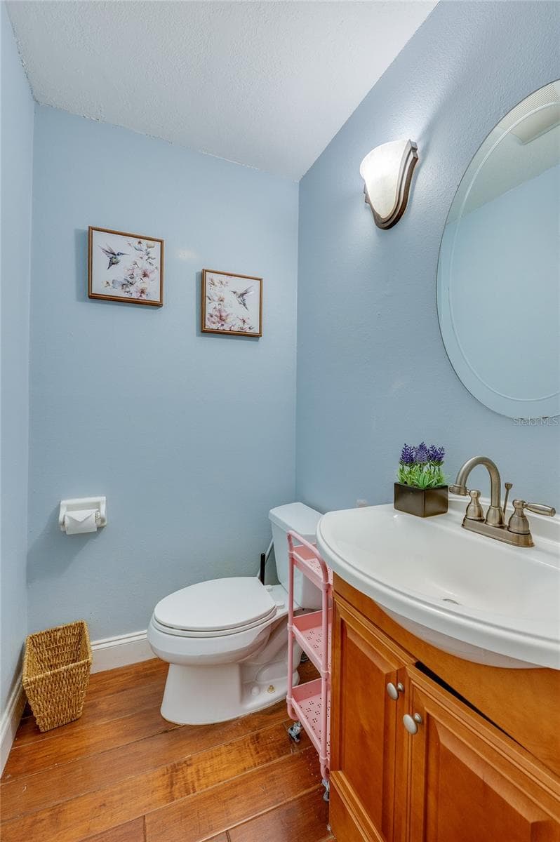 Charming half-bath featuring soft blue walls, a wooden vanity cabinet, oval mirror, and warm laminate flooring. - 2081 PENNSYLVANIA DR, DELAND