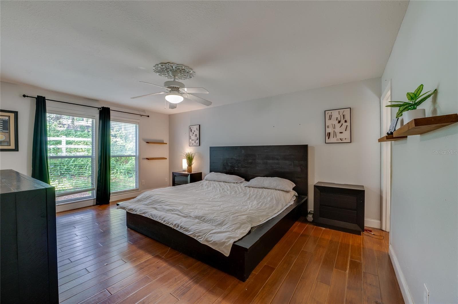 Spacious bedroom boasting warm laminate floors, large windows with full-length curtains, and a ceiling fan with light fixture. - 2081 PENNSYLVANIA DR, DELAND