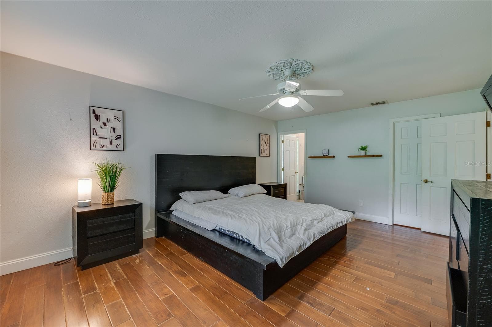 Comfortable master suite boasting rich laminate flooring, a central ceiling fan with ornate medallion molding, and direct access to an ensuite bathroom. - 2081 PENNSYLVANIA DR, DELAND