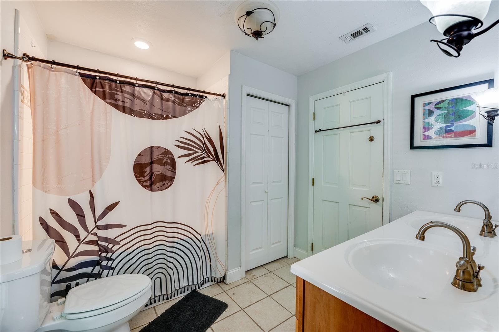 Full bathroom with tiled floors, a double-sink vanity with warm wood cabinetry, a tiled tub-shower combination, and a separate linen closet. - 2081 PENNSYLVANIA DR, DELAND