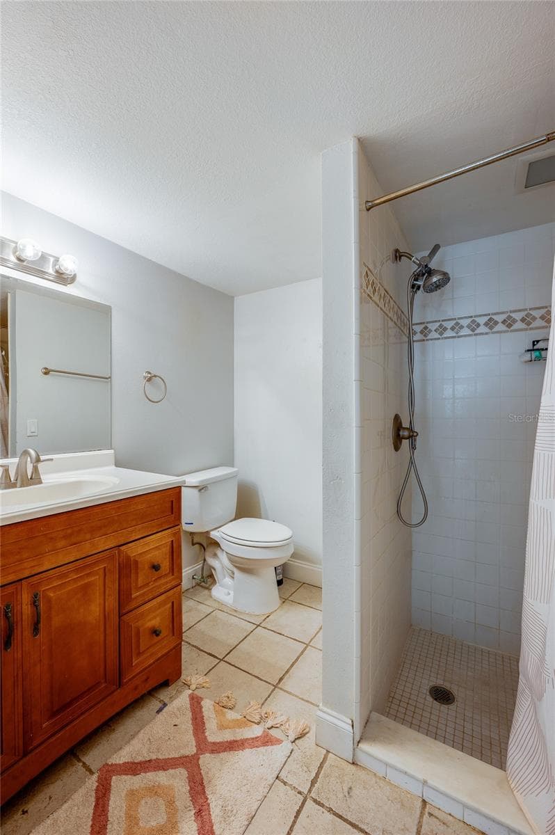 Compact bathroom with a tiled walk-in shower, warm wood vanity, single sink, and neutral ceramic tile flooring. - 2081 PENNSYLVANIA DR, DELAND