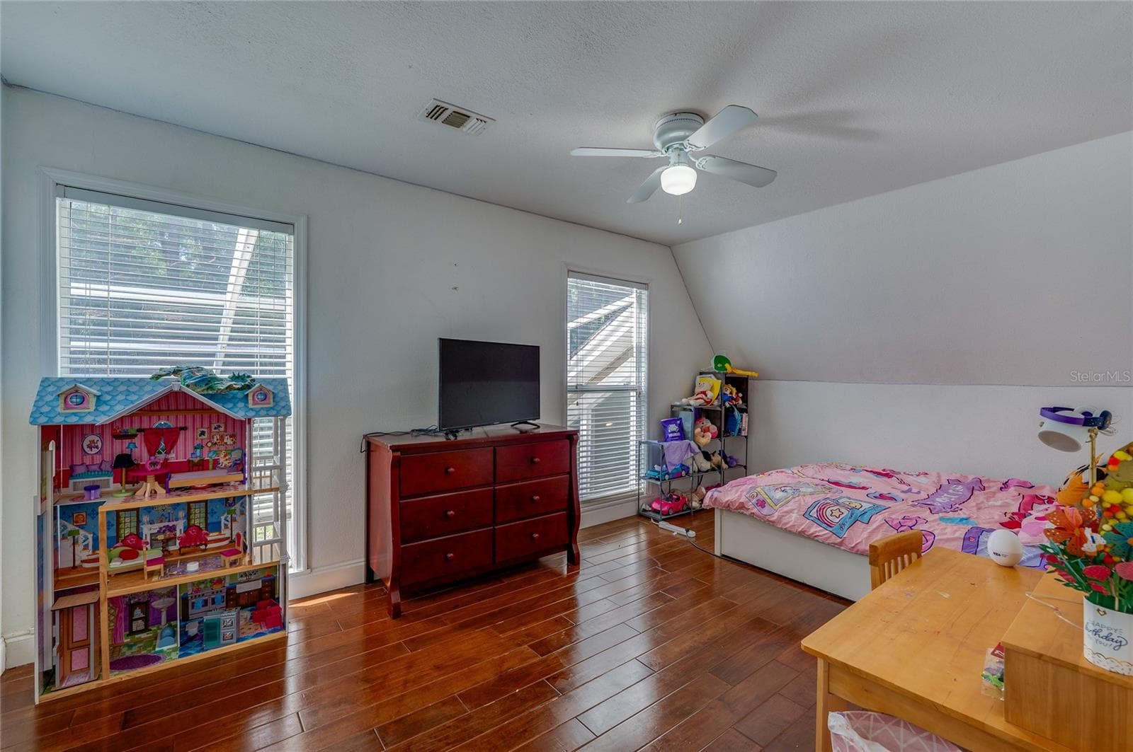 Bright bedroom featuring rich laminate flooring, a central ceiling fan, and sloped ceiling accents with dual windows. - 2081 PENNSYLVANIA DR, DELAND