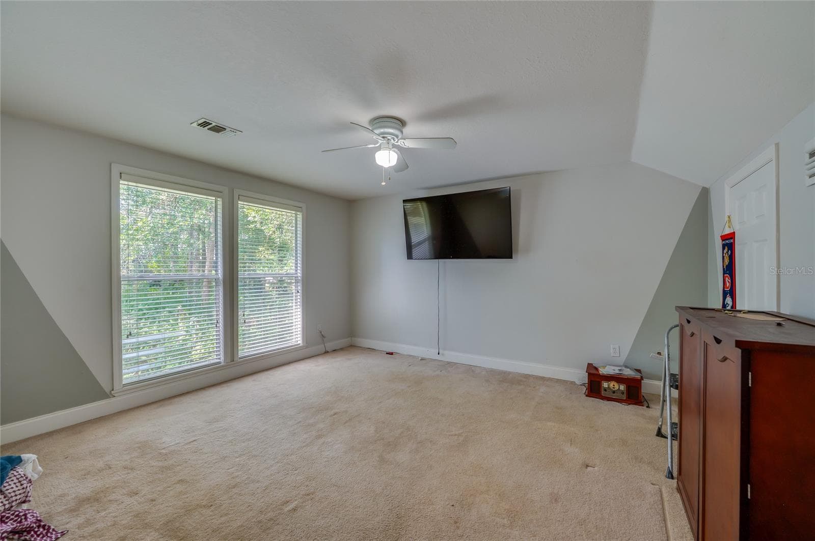 Spacious carpeted room featuring a white ceiling fan and large windows providing natural light. - 2081 PENNSYLVANIA DR, DELAND