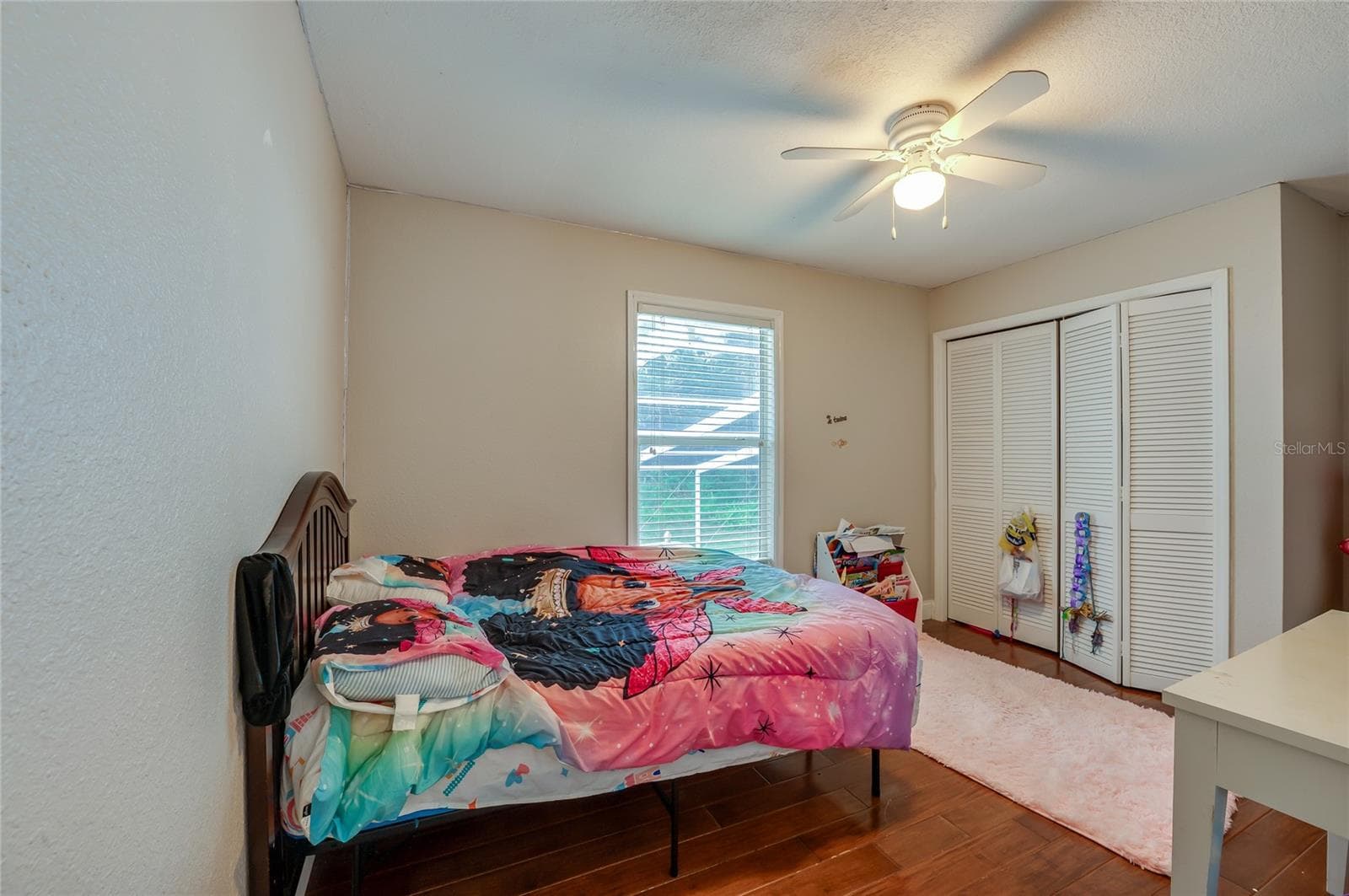 Cozy bedroom layout showcasing rich laminate floors, a central ceiling fan, and spacious closet doors. - 2081 PENNSYLVANIA DR, DELAND
