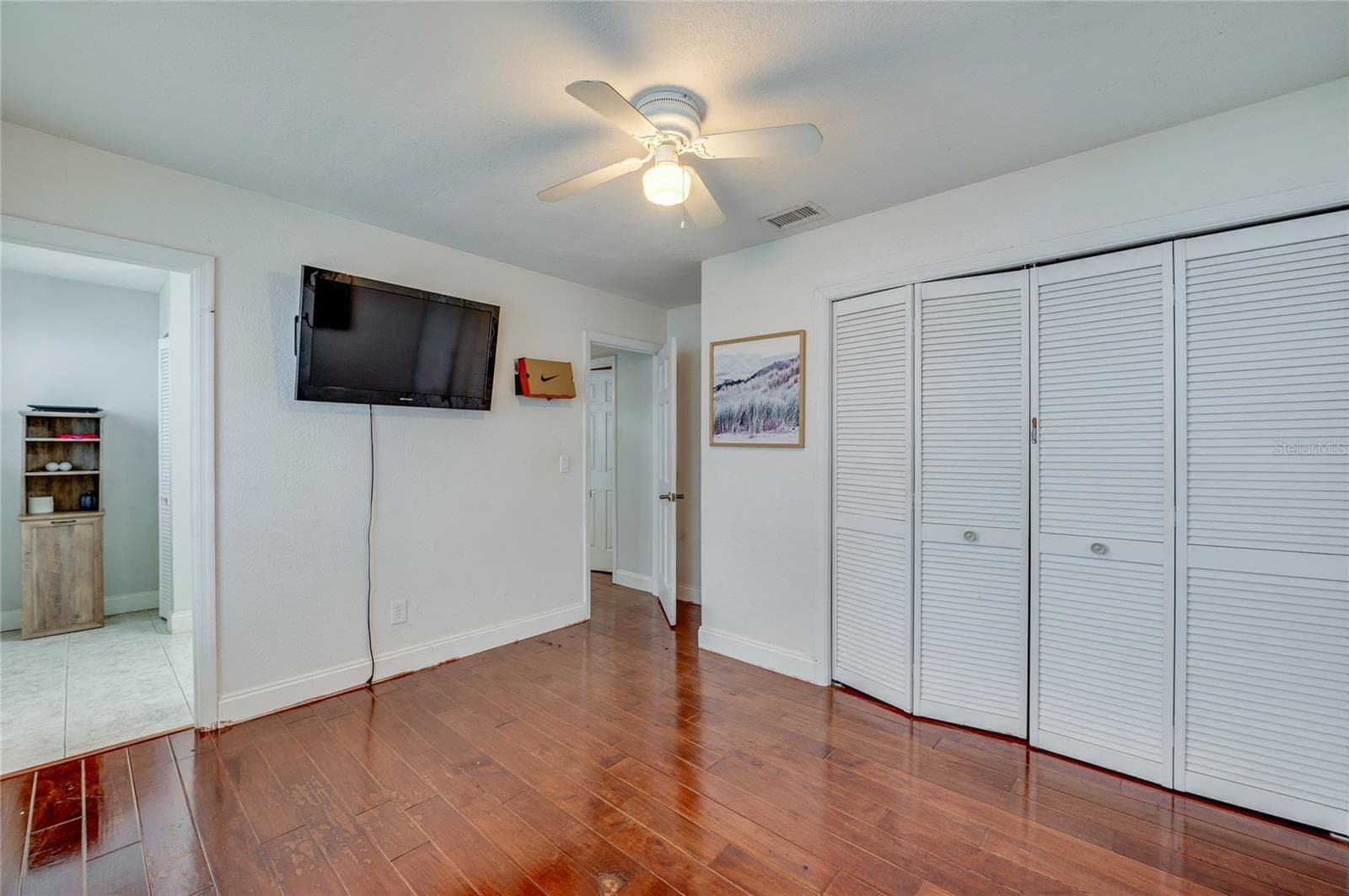Bright bedroom area highlighting rich dark laminate flooring, crisp white walls, a central ceiling fan, and closet doors. - 2081 PENNSYLVANIA DR, DELAND