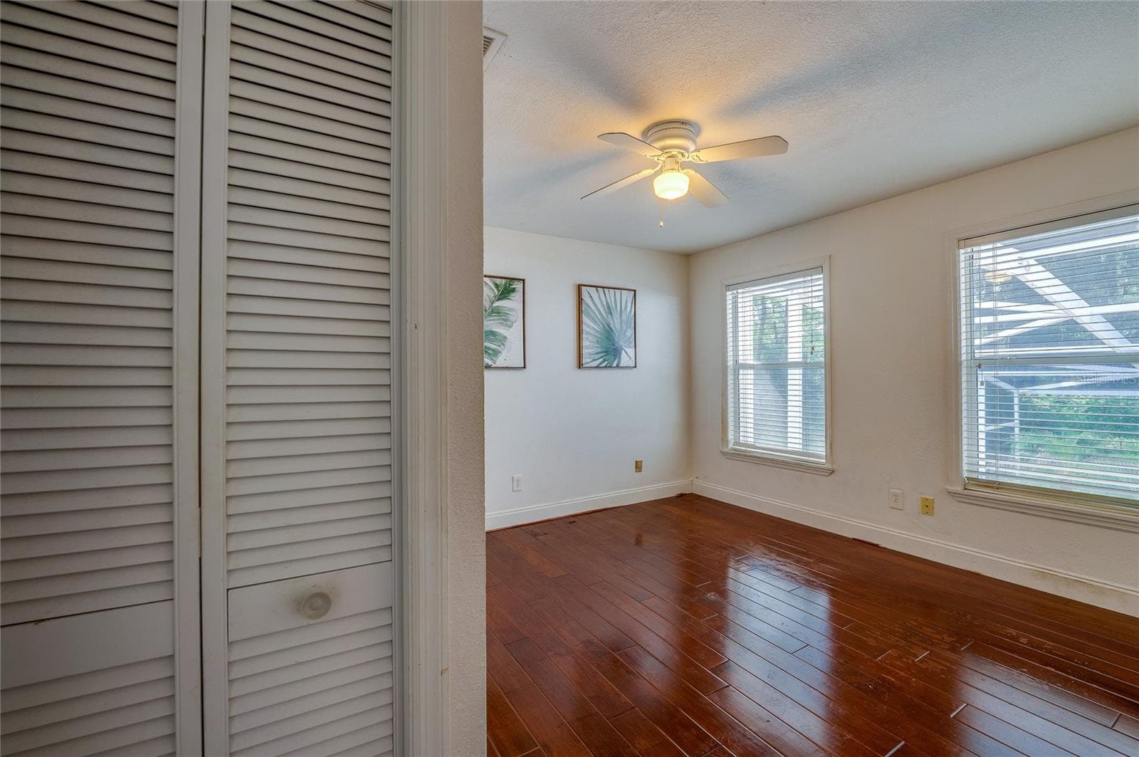 Sunlit bedroom space featuring rich laminate flooring, white wall trim, dual multi-pane windows, and a central ceiling fan. - 2081 PENNSYLVANIA DR, DELAND