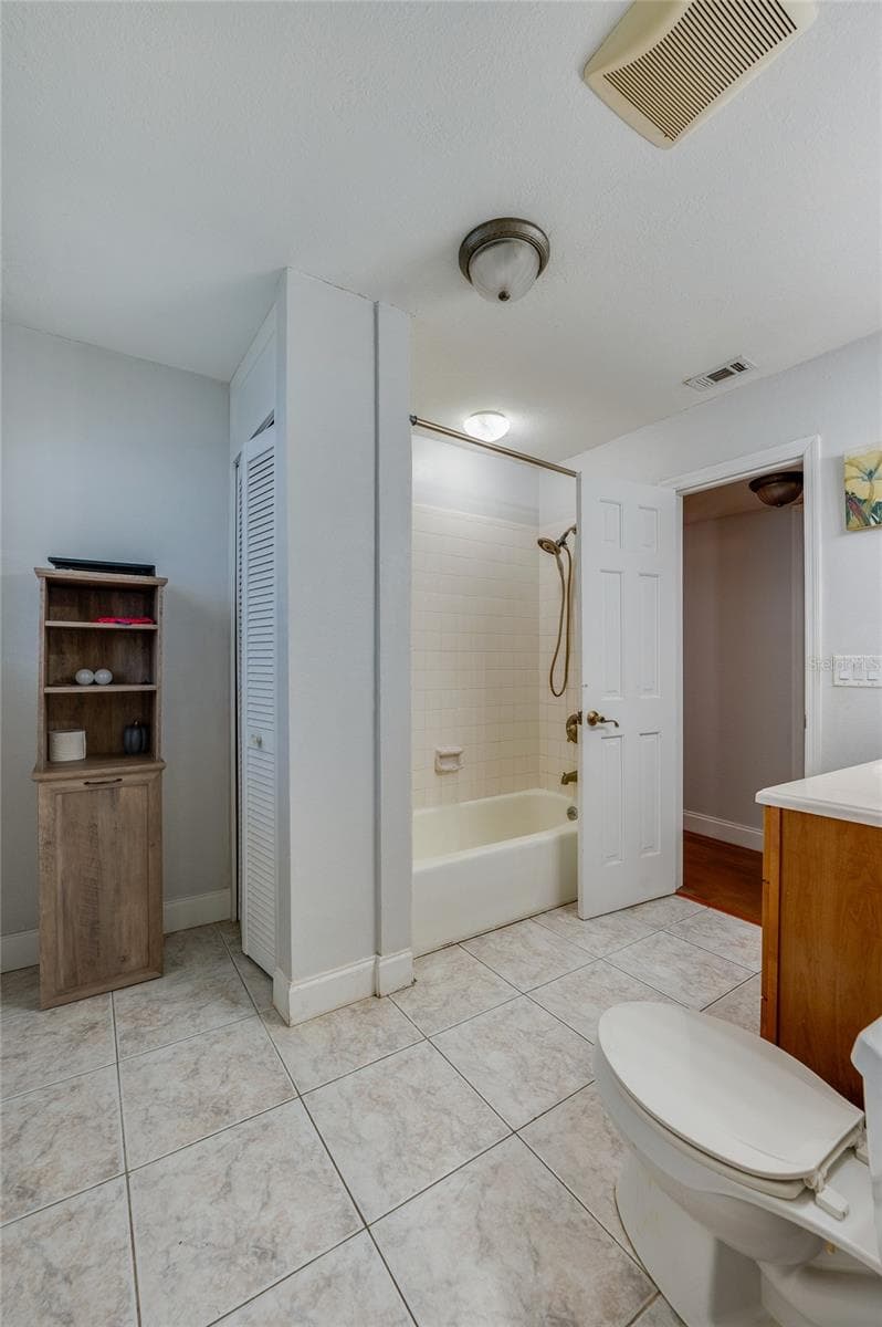 Tiled bathroom space highlighting a shower-tub combination, a white paneled interior door, and built-in closet storage. - 2081 PENNSYLVANIA DR, DELAND