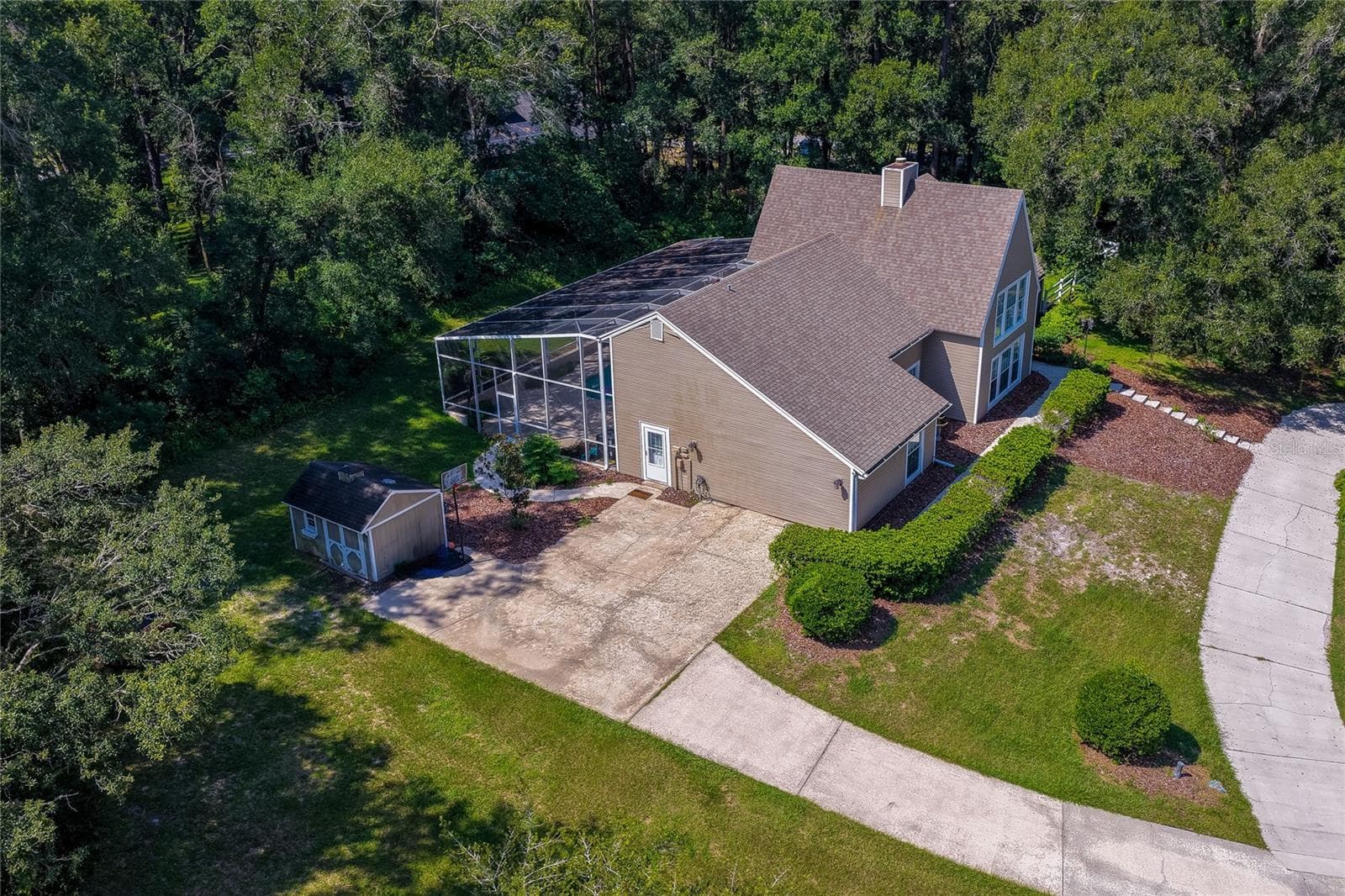 High-angle aerial view of the home showing its screened pool enclosure, side concrete parking pad, storage shed, and surrounding forest canopy. - 2081 PENNSYLVANIA DR, DELAND