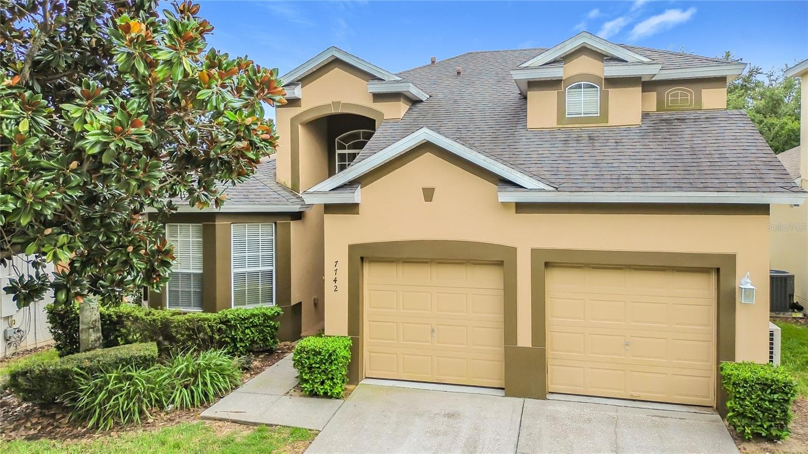 Beautiful front elevation with mature landscaping and a two-car garage. - 7742 COMROW ST, KISSIMMEE