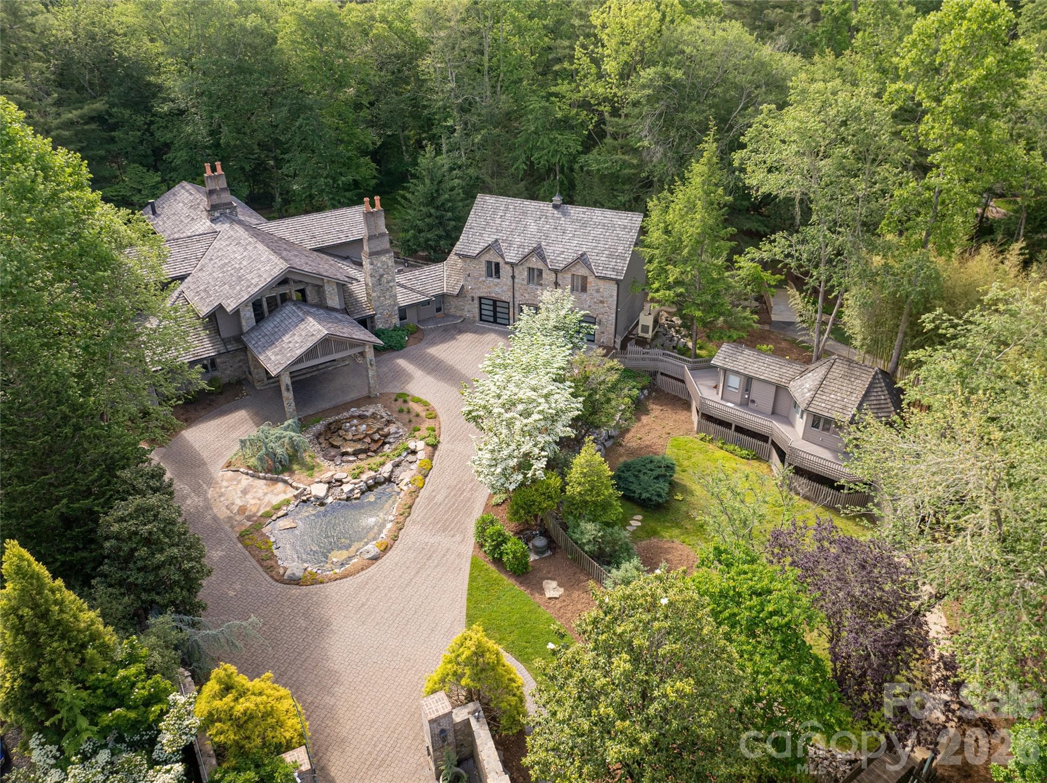 The six-bedroom main house, nestled in a serene forest setting, is seamlessly connected to one of two charming guest cottages and welcomes you with a circular driveway and a picturesque pond and fountain. - Asheville