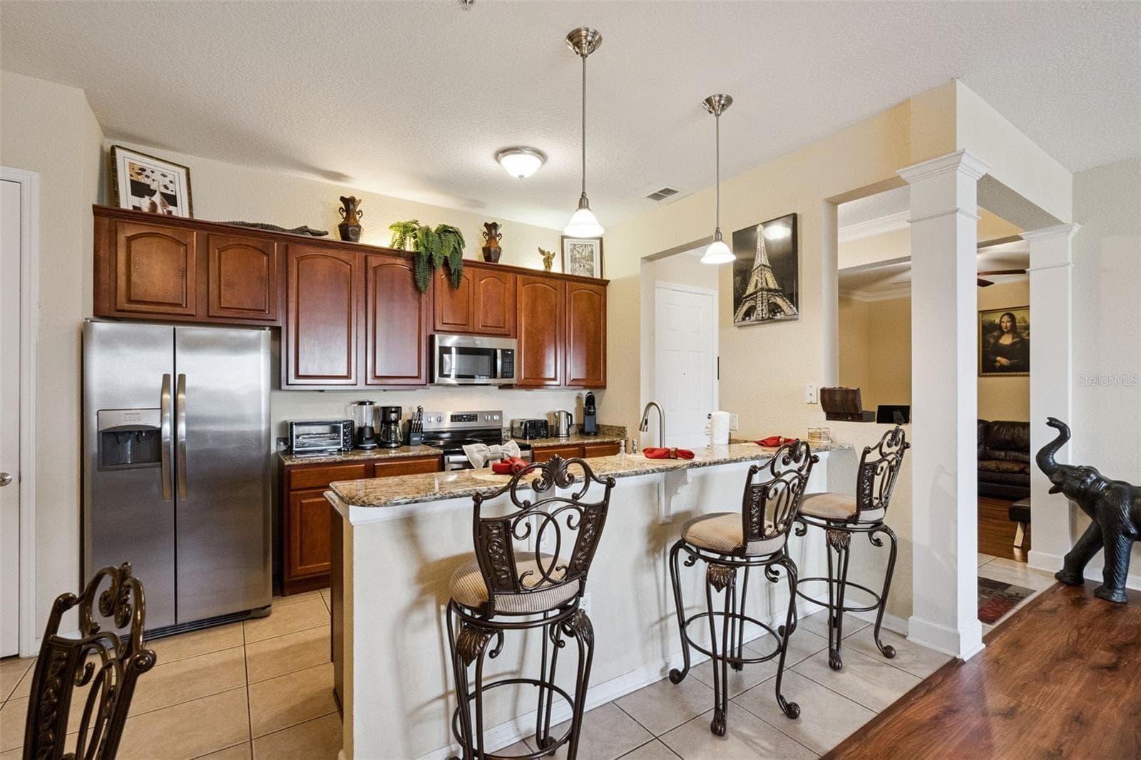 Kitchen & Dining Perspective:Side angle highlighting the full kitchen layout, side-by-side stainless steel refrigerator, raised breakfast bar, tile flooring, and wood-floored transition space. - 4840 CAYVIEW AVE #405, ORLANDO