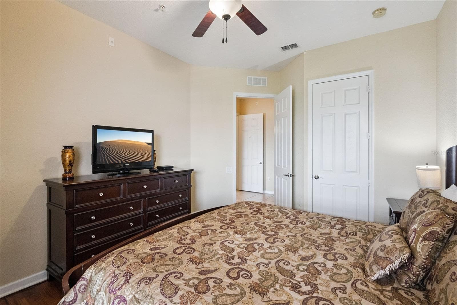 Bedroom Dresser Perspective:Perspective of the bedroom showing the matching dark wood dresser, flat-screen TV setup, wood-look flooring, and door leading out to the main hallway. - 4840 CAYVIEW AVE #405, ORLANDO