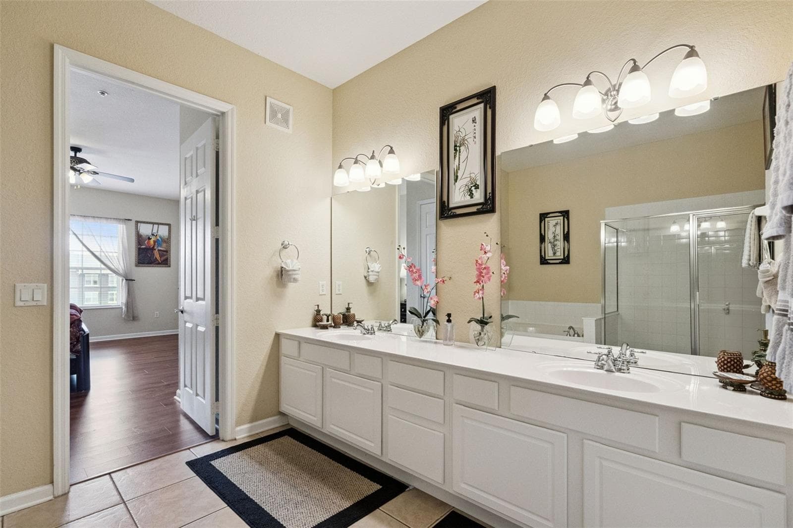 Primary Bath Entrance View:Wide perspective of the en-suite bathroom highlighting the extended double vanity, bright lighting fixtures, tiled floor, and seamless doorway connection to the primary suite. - 4840 CAYVIEW AVE #405, ORLANDO