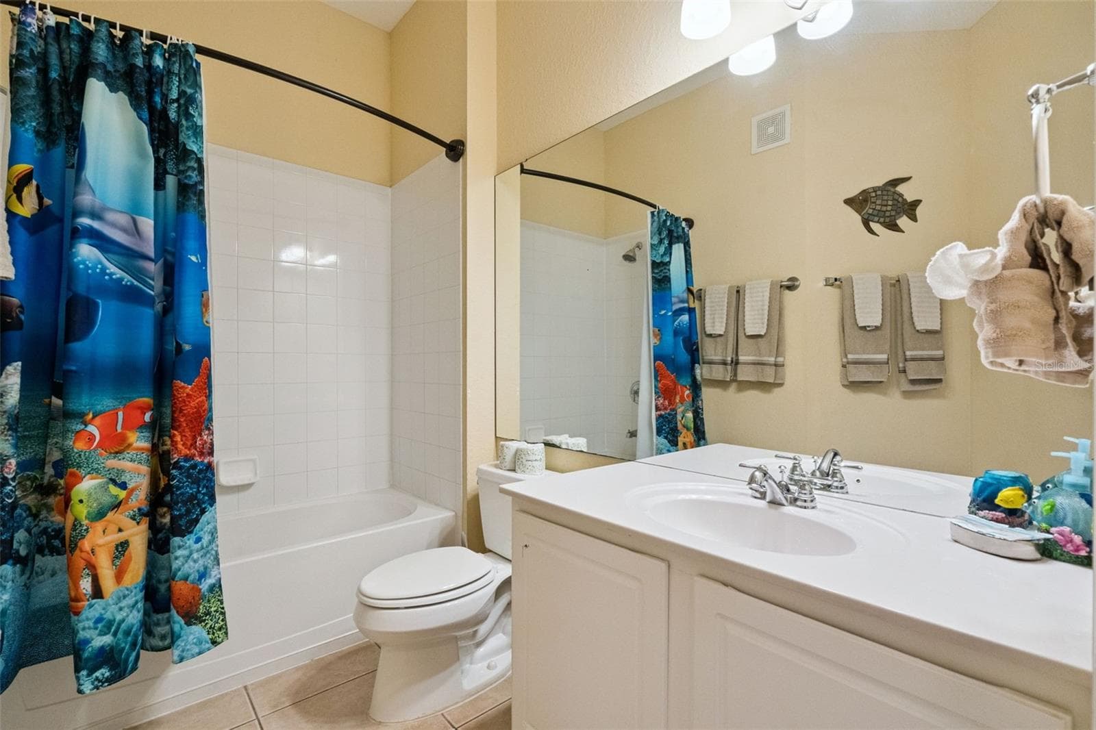 Guest Bathroom:Bright guest bathroom featuring a white single-sink vanity, full-width mirror, tile flooring, and a tub/shower combination with tile surround. - 4840 CAYVIEW AVE #405, ORLANDO
