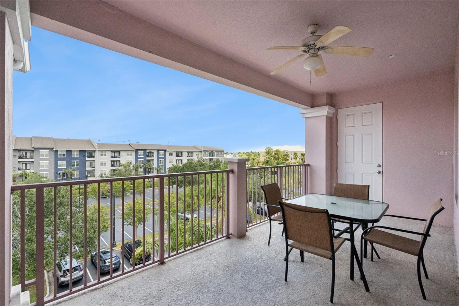 Balcony & Exterior Access:Spacious covered porch area offering outdoor seating, ceiling fan, exterior utility door access, and views of the parking area and greenery. - 4840 CAYVIEW AVE #405, ORLANDO
