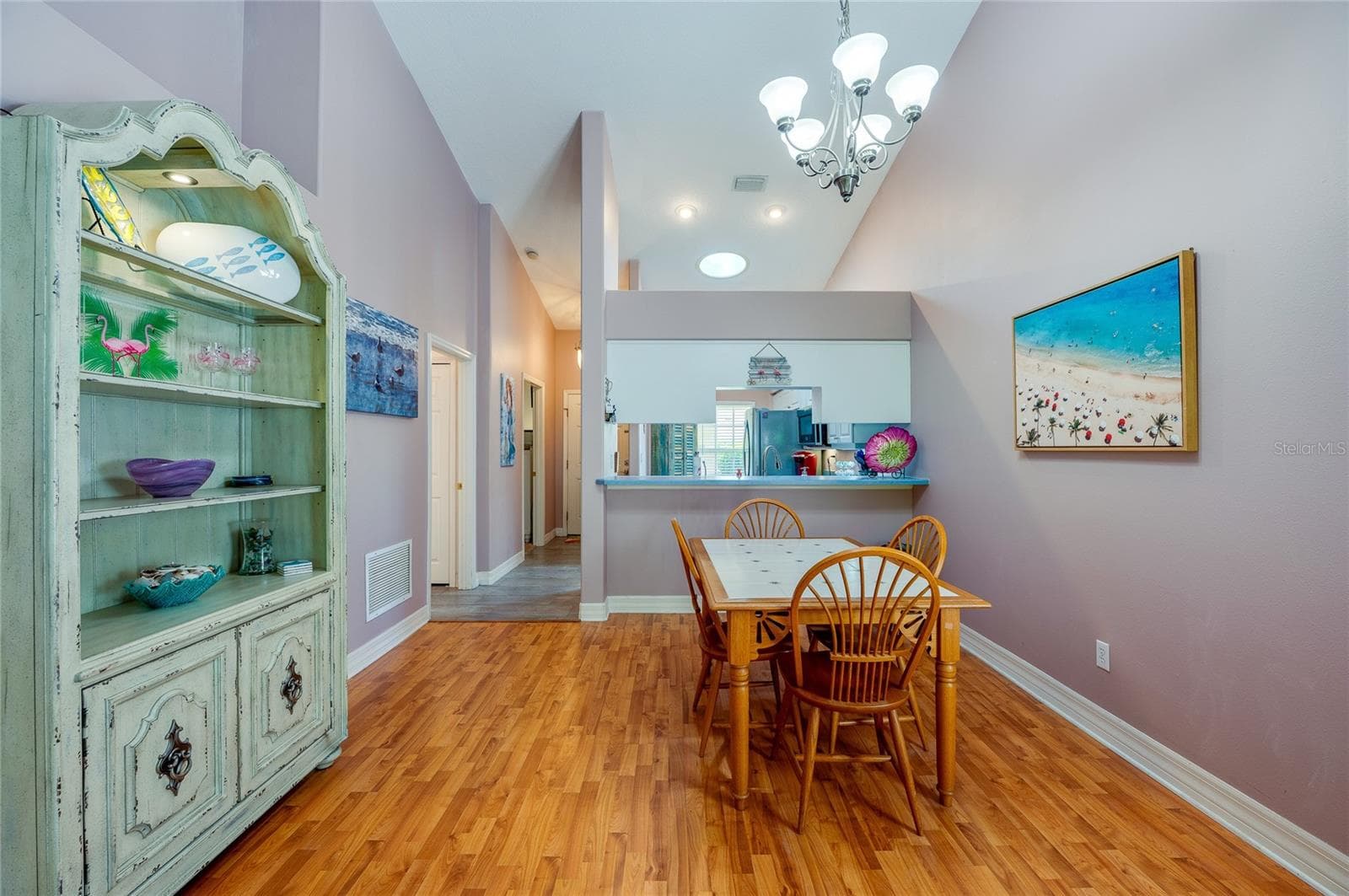 Open dining space featuring rich laminate flooring, high vaulted ceilings, and a central chandelier. A cutout wall provides a direct view into the kitchen, enhancing the overall flow. - 1413 COCONUT PALM CIR, PORT ORANGE