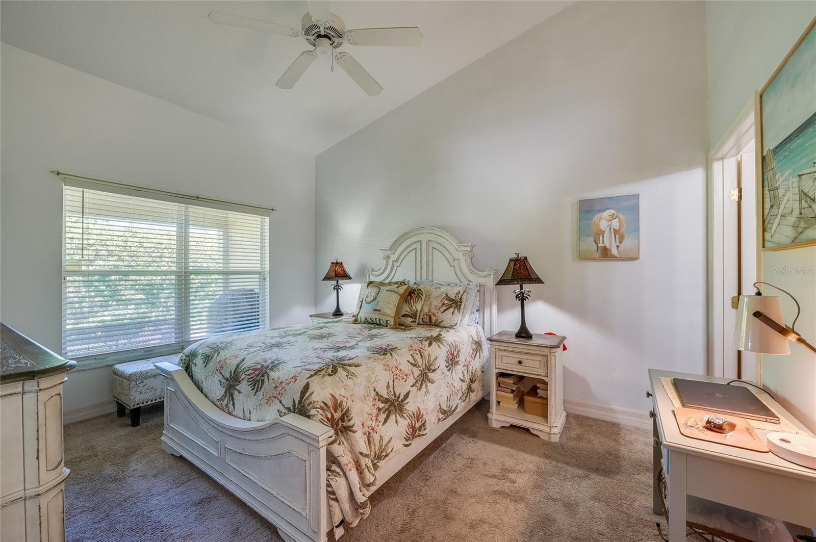 Serene bedroom suite featuring vaulted ceilings, soft neutral wall tones, and plush carpeting. A large window with horizontal blinds fills the room with indirect light. - 1413 COCONUT PALM CIR, PORT ORANGE