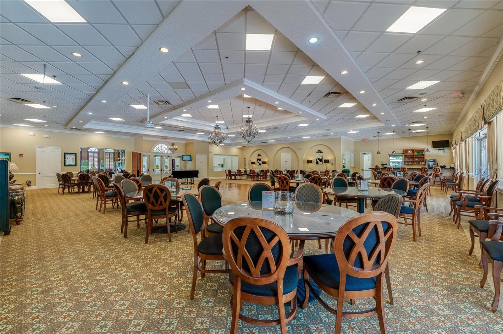 Wide perspective of the ballroom highlighting geometric drop ceilings, integrated lighting, and patterned carpeting that extends across the floor. Arched architectural elements and curtained glass doors line the perimeter walls. - 1413 COCONUT PALM CIR, PORT ORANGE