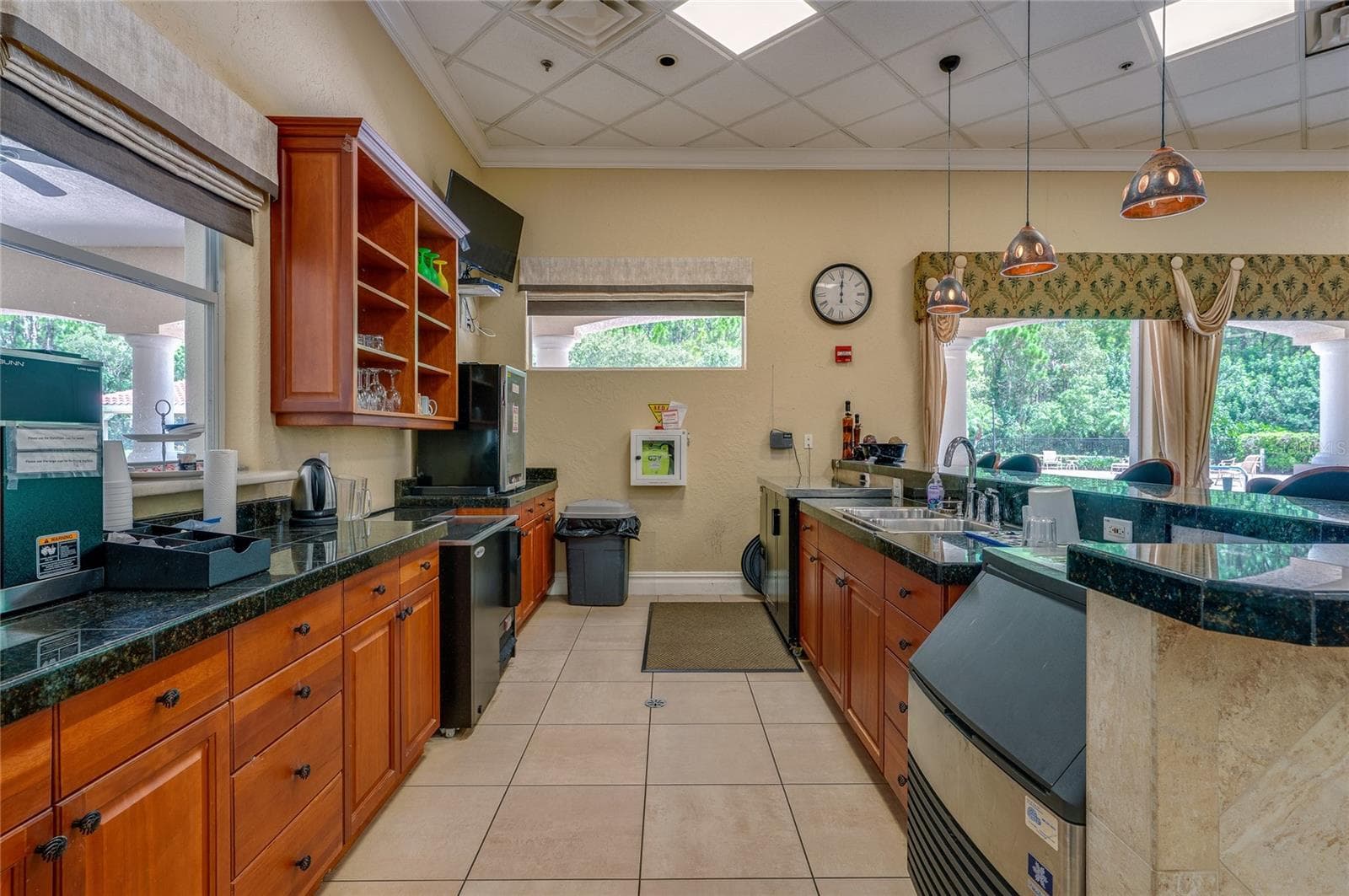 Functional beverage station and service kitchen equipped with extensive dark granite countertops, rich wood cabinetry, stainless steel sink stations, and tile flooring. Wide windows and valanced drapery overlook the outdoor grounds. - 1413 COCONUT PALM CIR, PORT ORANGE