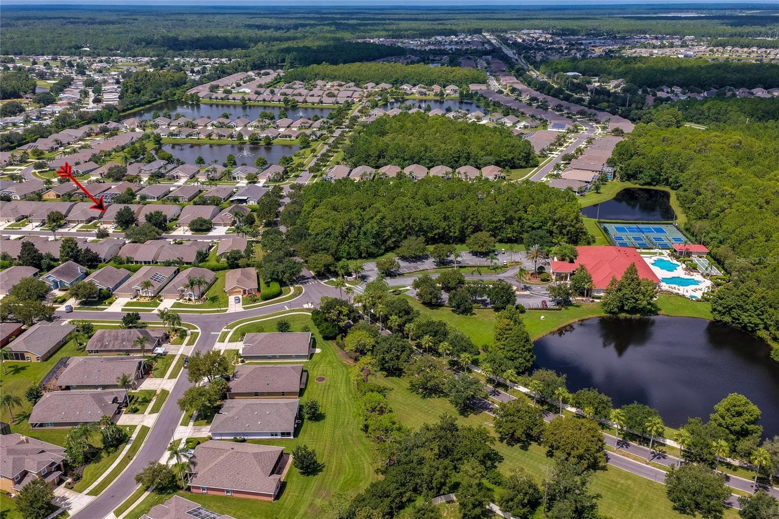 Sweeping neighborhood aerial displaying quiet residential streets lined with single-story homes, tranquil ponds, and lush green common areas. An indicator arrow marks a specific residence within the scenic layout. - 1413 COCONUT PALM CIR, PORT ORANGE