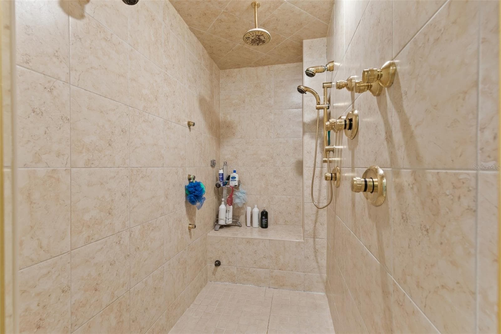 The fully-tiled walk-in shower has a bench and multiple showerheads. - 4603 DOGWOOD HILLS CT, BRANDON