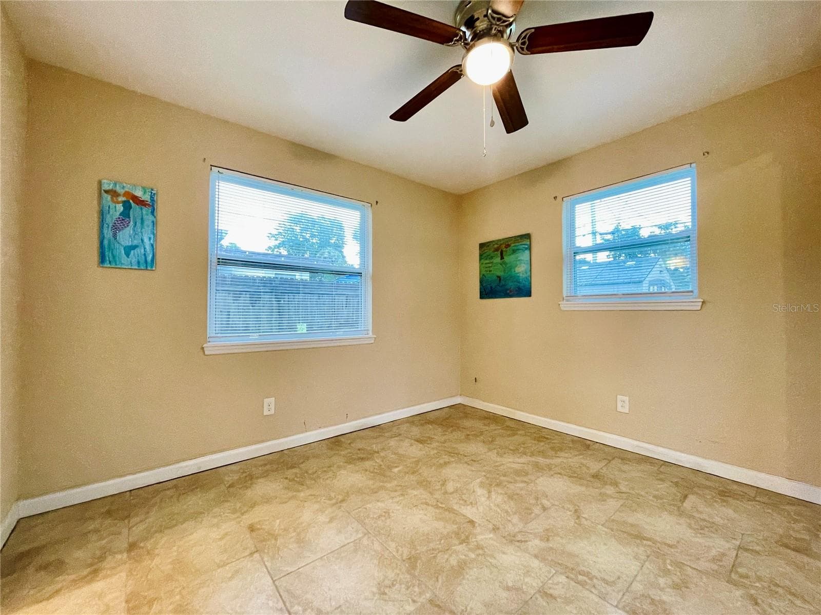 Cozy bedroom featuring warm tan walls, tile flooring, and ample natural light from two windows. - 723 STEELE AVE, SOUTH DAYTONA