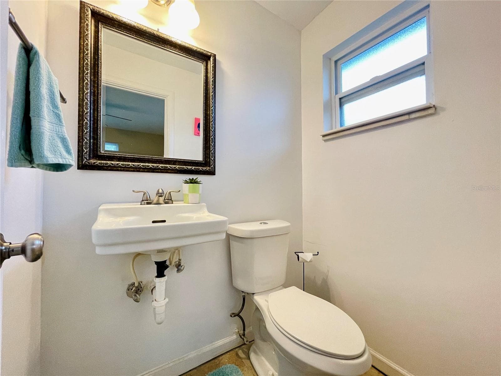 Functional half-bathroom off the bedroom with equipped with a classic wall-mounted sink, a decorative framed mirror, and a frosted privacy window. - 723 STEELE AVE, SOUTH DAYTONA