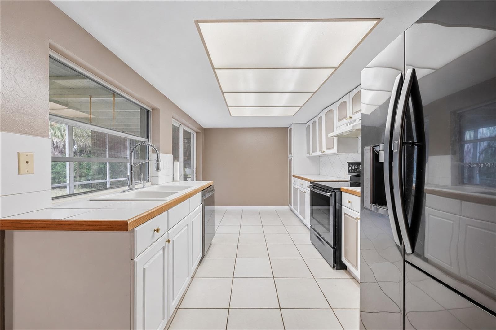 Open-concept kitchen highlighting white cabinetry, stainless steel refrigerator, tile backsplash, and pass-through window to the lanai. - 3906 SANTIAGO ST, SEBRING