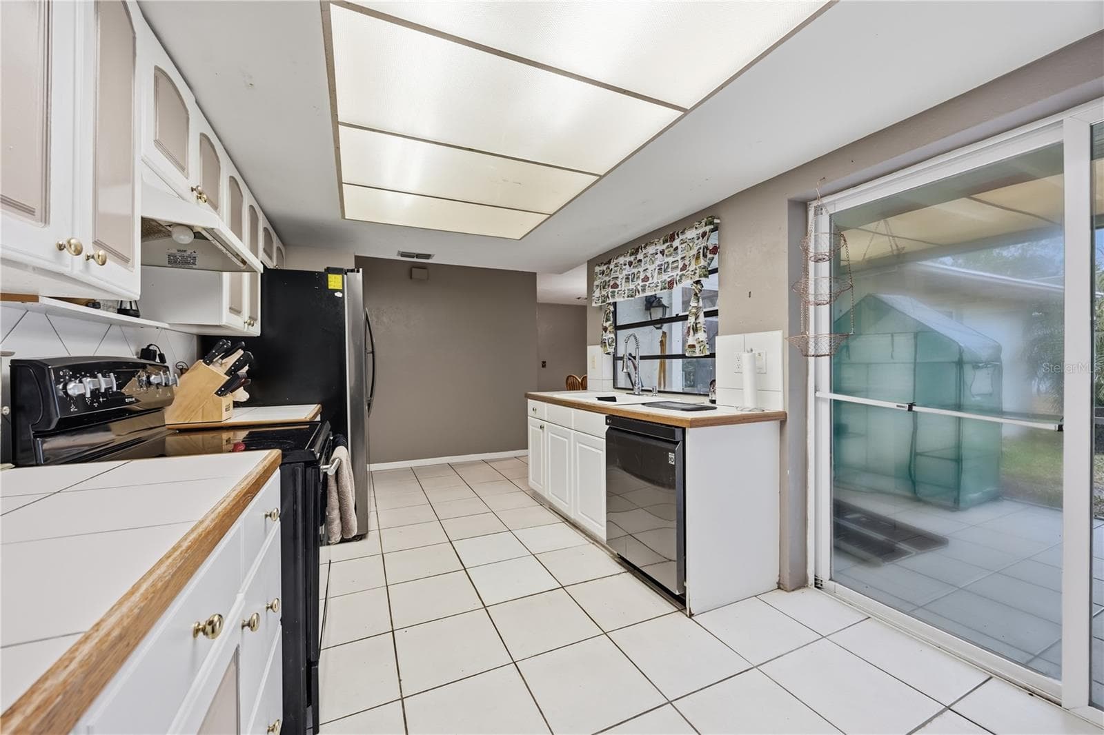 Functional kitchen featuring white cabinetry, tile flooring, updated appliances, and sliding glass door access directly to the screened lanai. - 3906 SANTIAGO ST, SEBRING