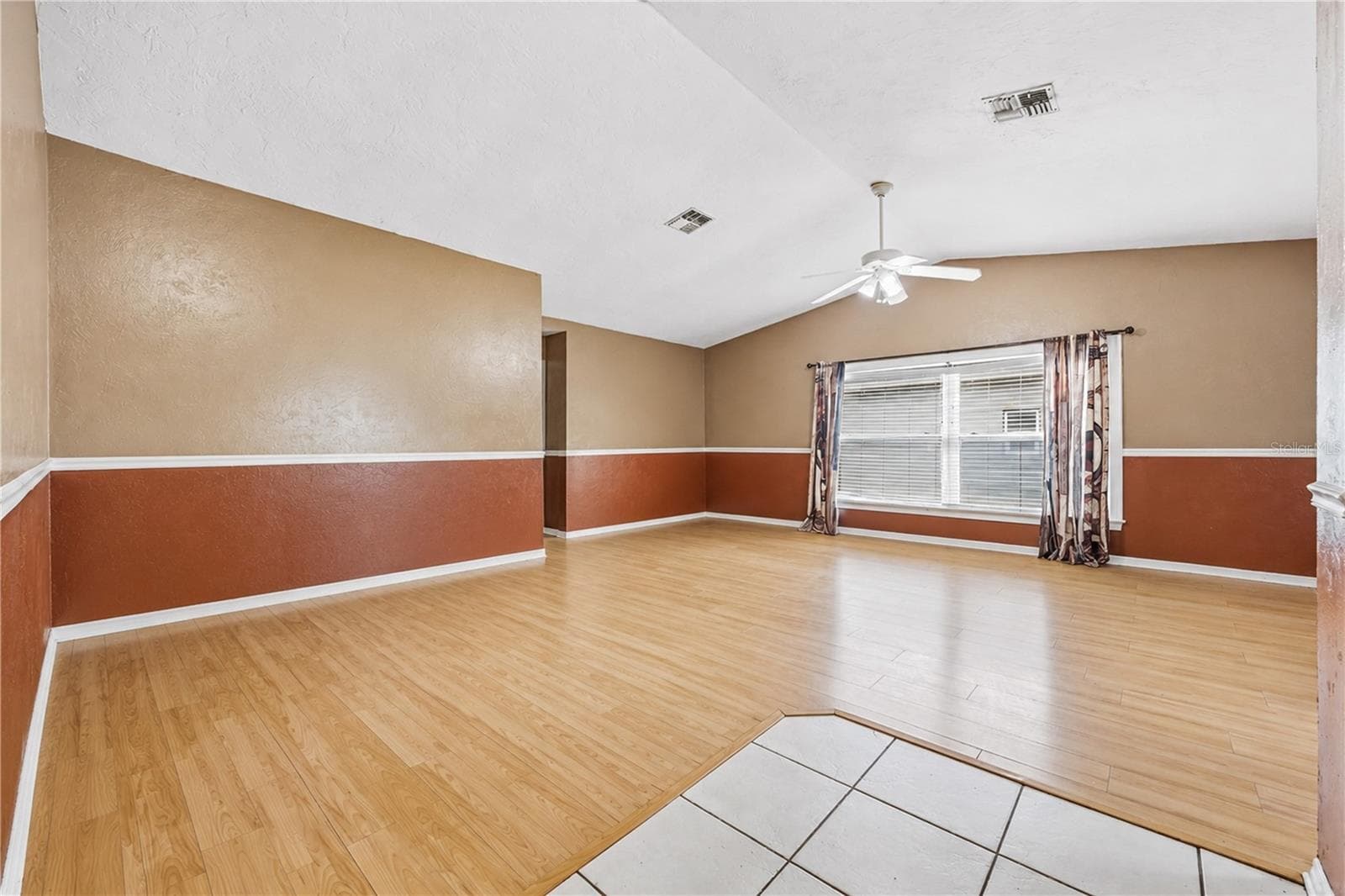 Spacious open living room featuring vaulted ceilings, light wood-look flooring, ceiling fan, and abundant natural light. - 3906 SANTIAGO ST, SEBRING