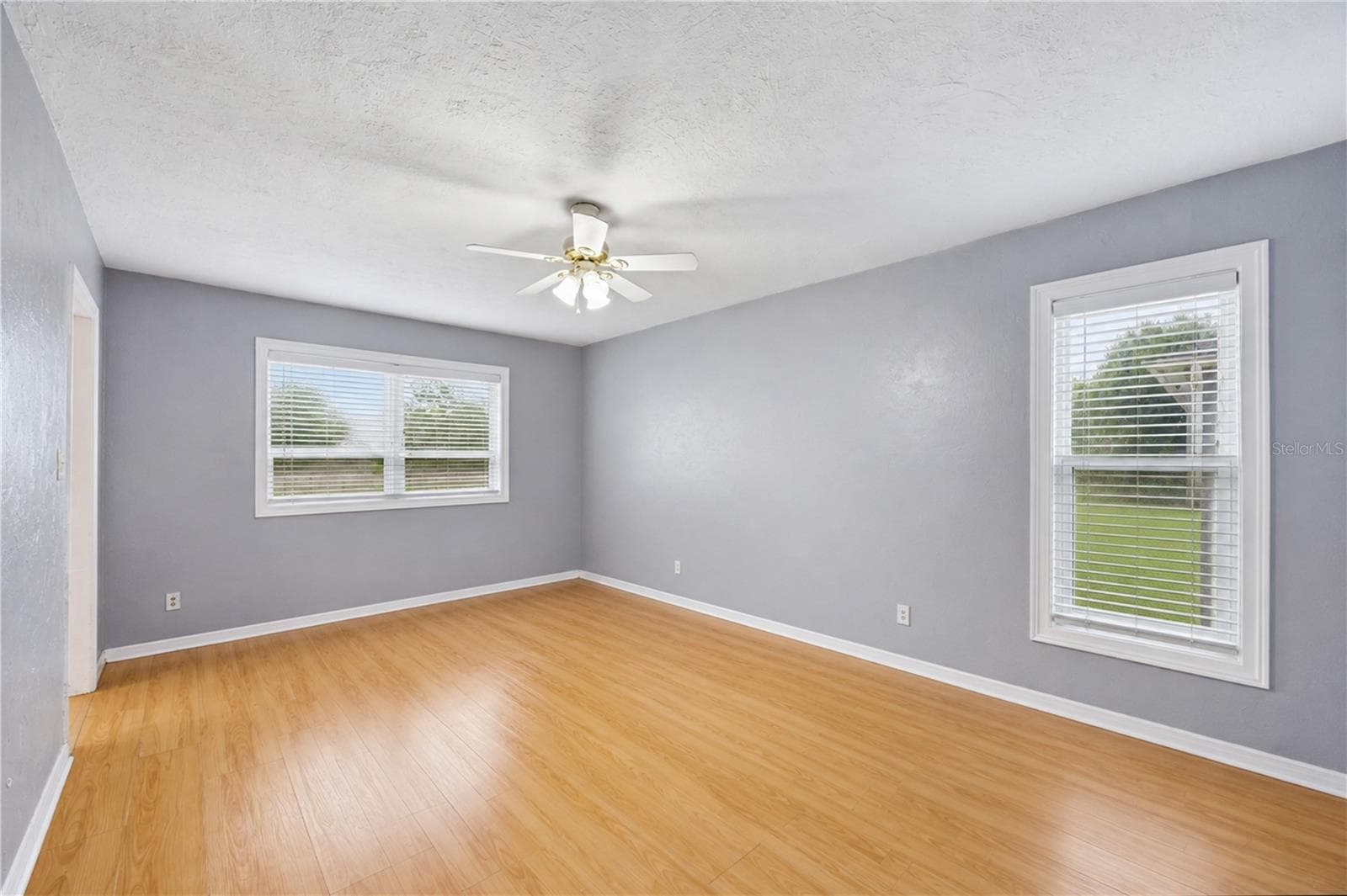 Primary suite offering continuous wood-look flooring, neutral grey palette, ceiling fan, and dual windows. - 3906 SANTIAGO ST, SEBRING