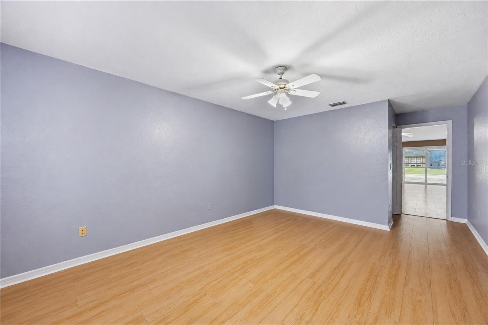 Large primary bedroom with continuous wood-look flooring, ceiling fan, neutral grey walls, and dual windows for abundant natural light. - 3906 SANTIAGO ST, SEBRING