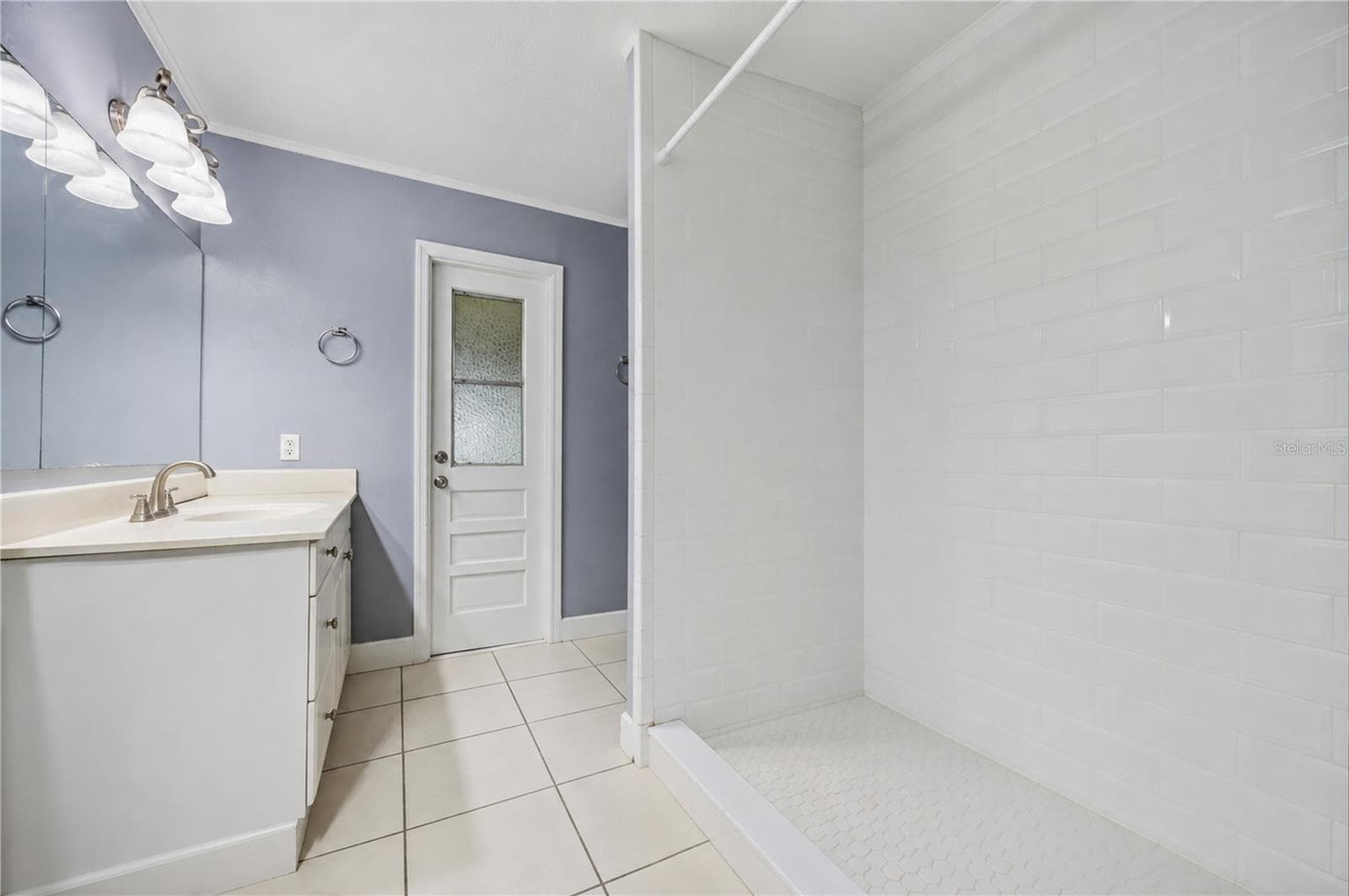 Ensuite bathroom updated with a modern white subway-tiled walk-in shower, large vanity, and privacy-glass door. - 3906 SANTIAGO ST, SEBRING