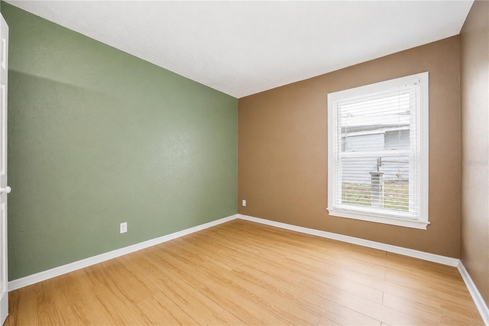 Bright bedroom with low-maintenance wood-look laminate flooring, accent wall, and a large window providing ample natural light. - 3906 SANTIAGO ST, SEBRING