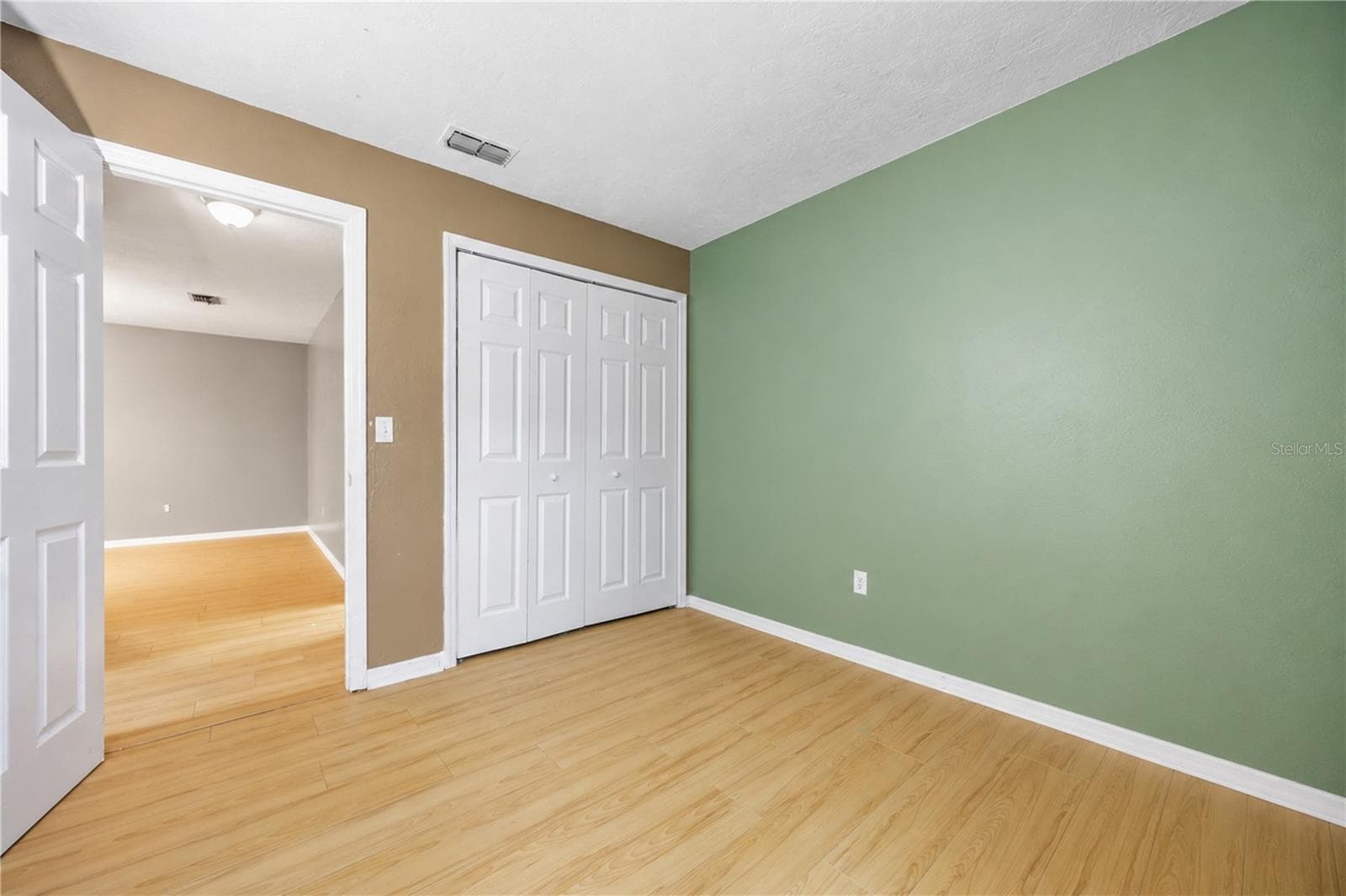 Secondary bedroom view highlighting clean lines, laminate flooring, double bi-fold closet doors, and smooth flow into the hallway. - 3906 SANTIAGO ST, SEBRING